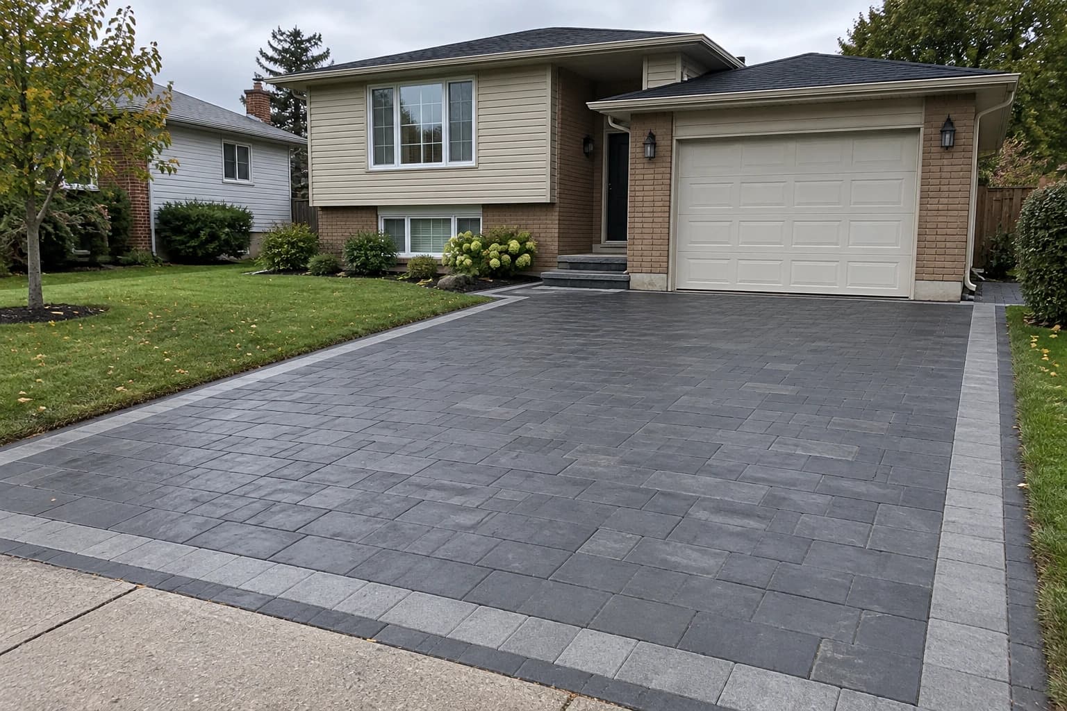 Charcoal interlock driveway with a light grey border in front of a split-level home
