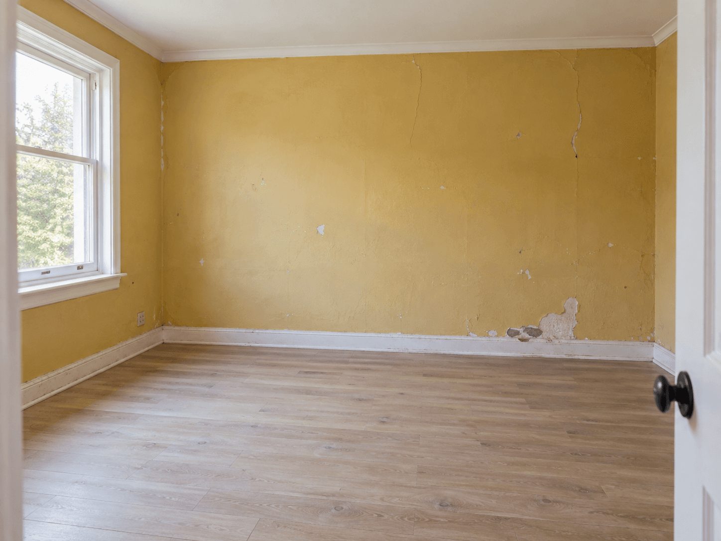 Empty room with cracked, peeling plaster walls before drywall work