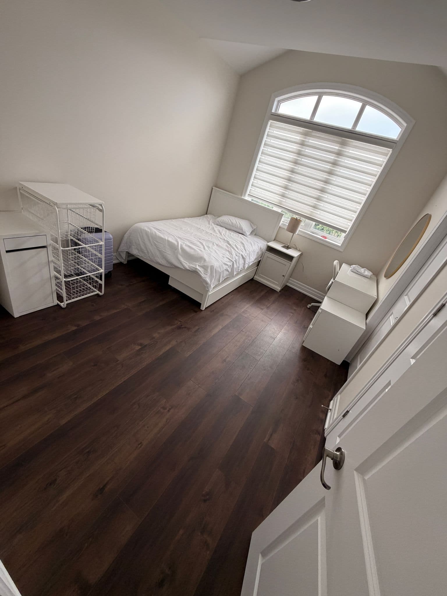 Dark plank flooring in a bedroom with a vaulted ceiling and arched window