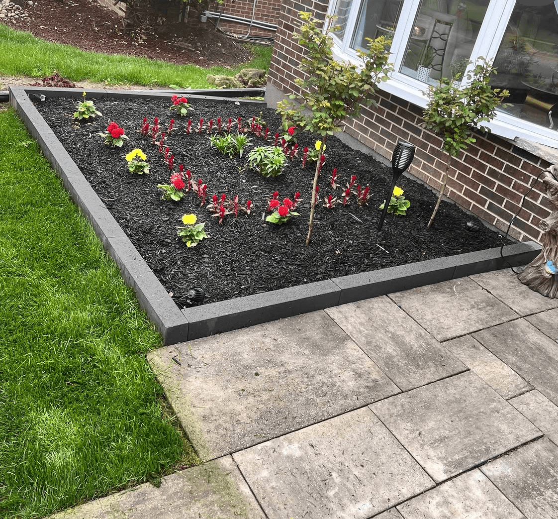 Finished garden bed with fresh mulch, flowers and a stone border against the house