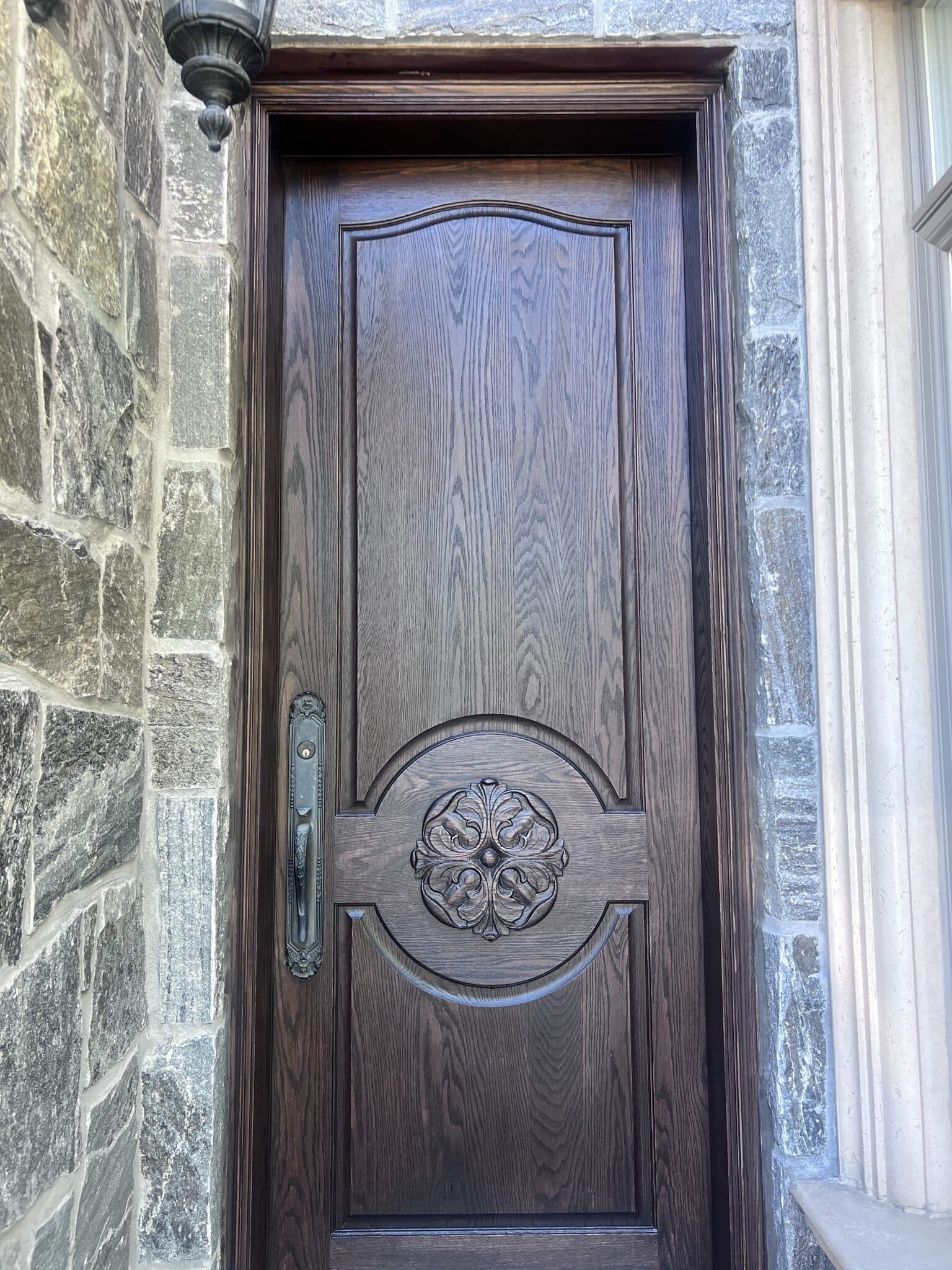 Carved oak entry door refinished in dark stain, set in a stone wall